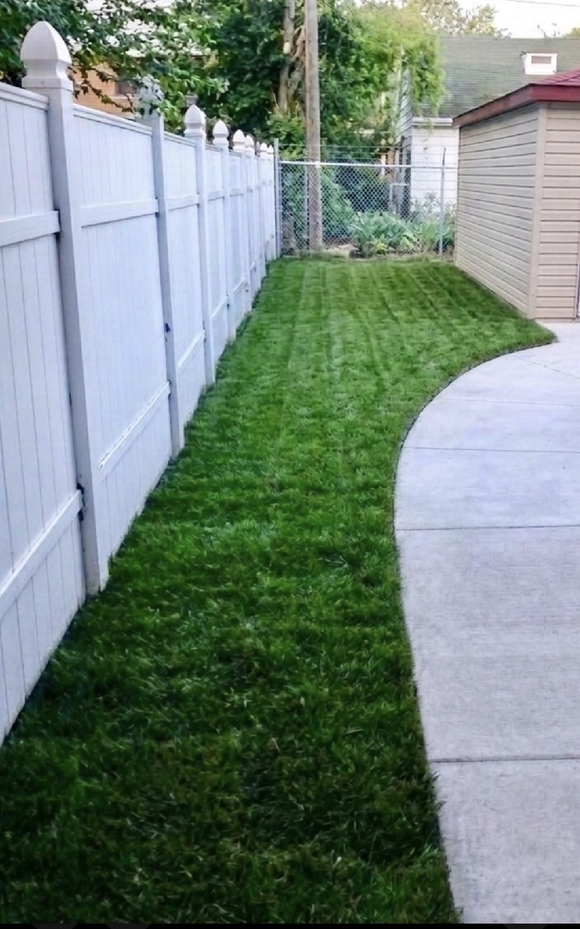 Lush green lawn maintained along a white fence line beside a walkway